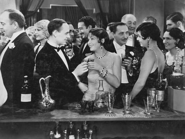 People dressed in tuxedos and dresses enjoying themselves in a fancy bar. 