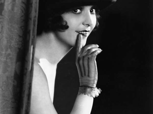 woman with a hat behind a curtain wearing a glove 