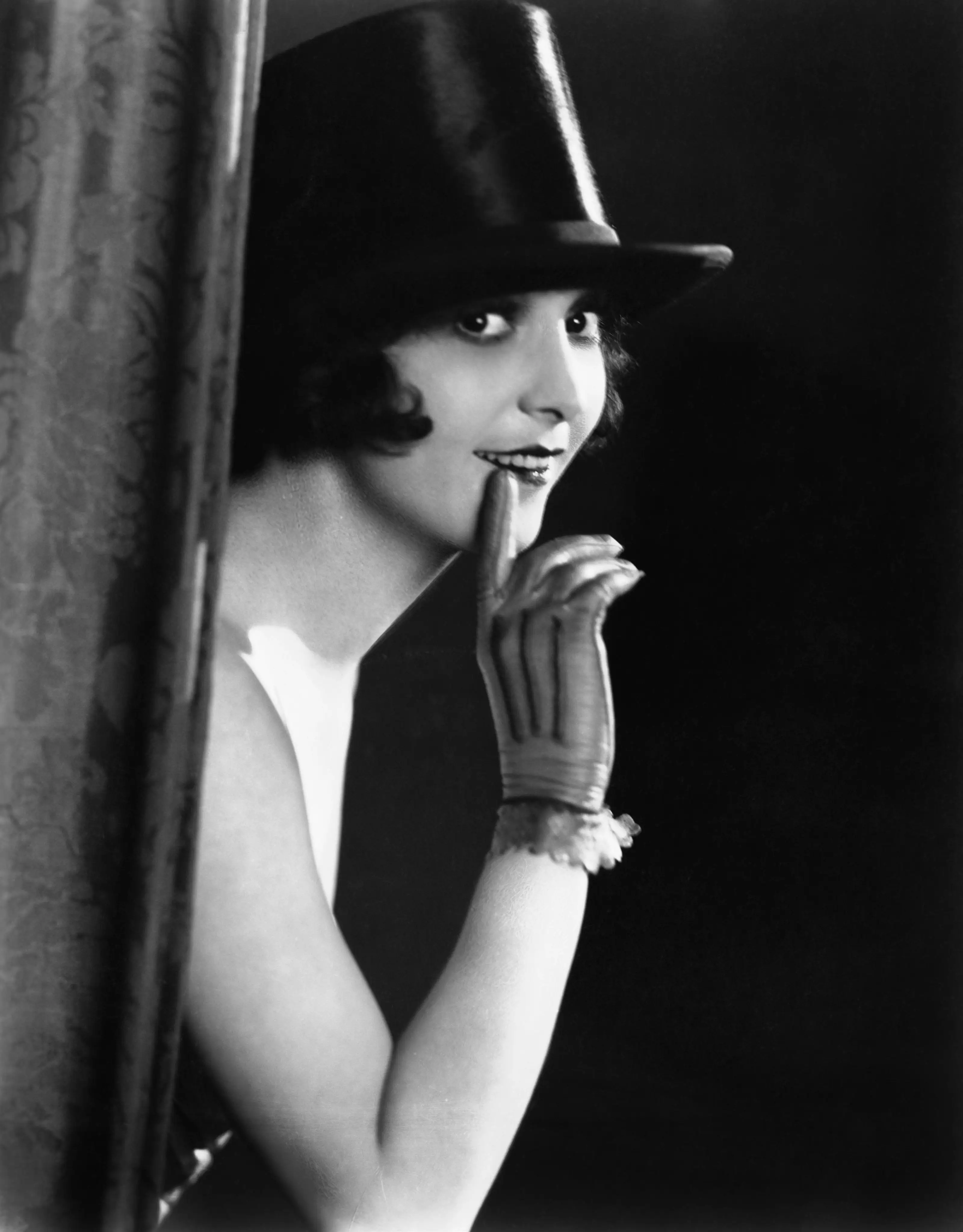 woman with a hat behind a curtain wearing a glove 